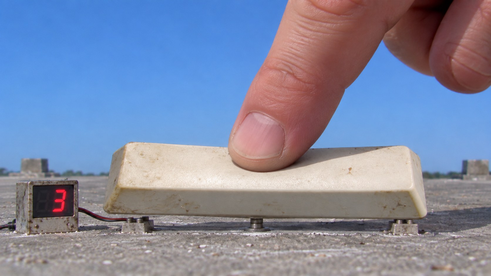 A huge finger pressing a spacebar on a miniature launch pad.